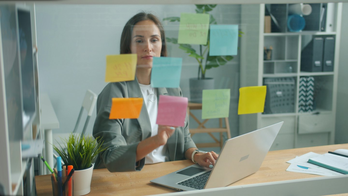 Woman organizes colorful sticky notes on a glass office partition.